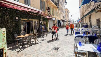 Una strada acciottolata con tavoli all'aperto, un ristorante con tenda rossa e un albergo con insegna.