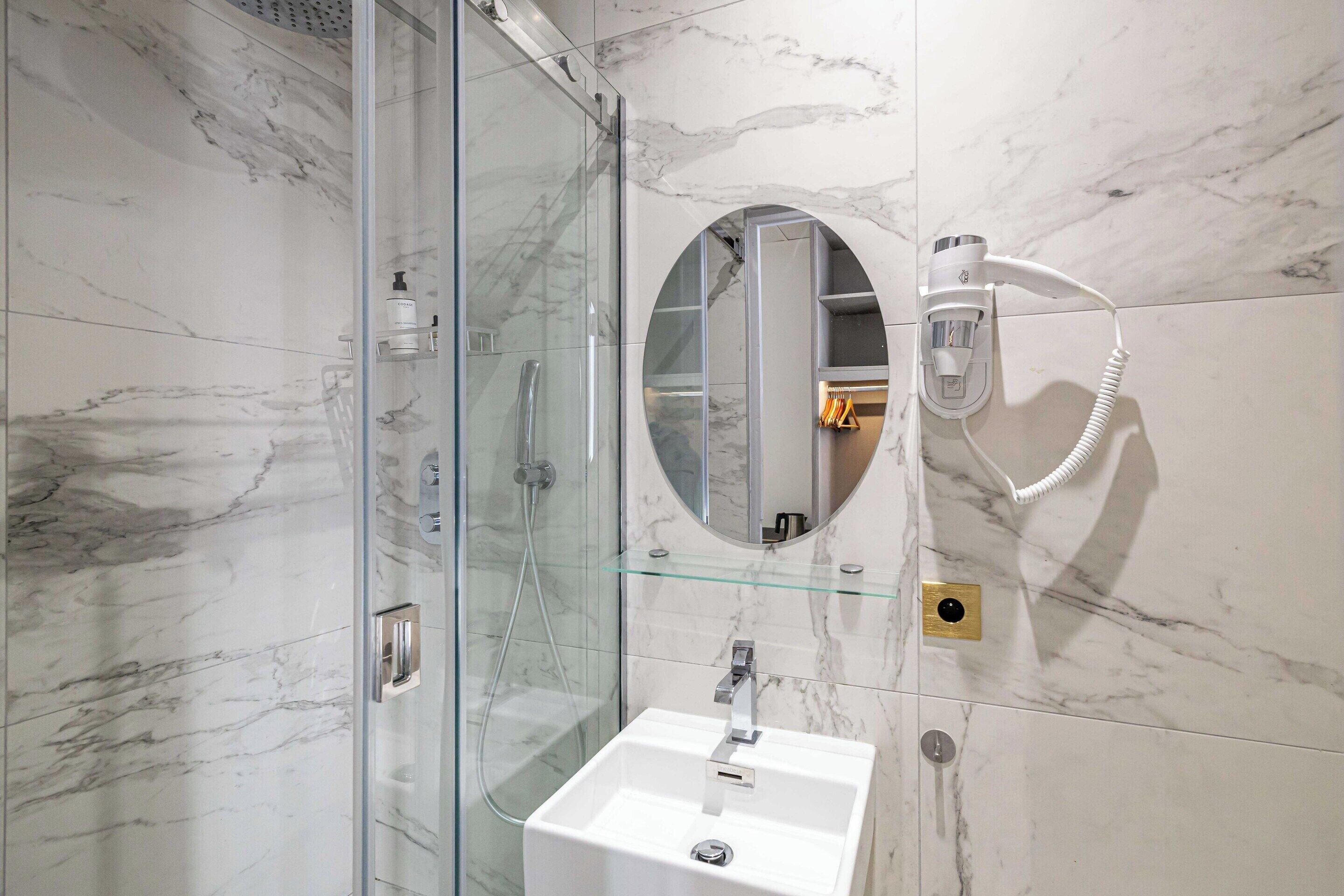 A modern bathroom with a glass-enclosed shower, a white sink, and a round mirror.