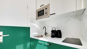 A compact kitchen with a built-in microwave, a sink, and a black induction cooktop. - Cosy Cocoon for 2P With A/C - Near Montmartre (Paris)