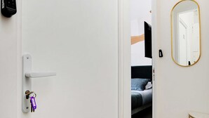 A hotel room with a white door, a keycard reader, a mirror, and a bed with a headboard. - Cosy Cocoon for 2P With A/C - Near Montmartre (Paris)