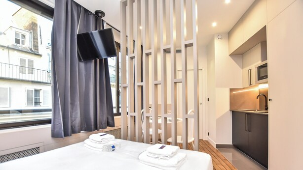 Una habitación de hotel moderna con cama, televisión, zona de cocina y vistas al exterior.