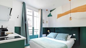 A modern bedroom with a bed, bedside table, and a built-in kitchen area.