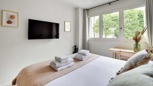 A hotel room with a bed, a TV mounted on the wall, a desk, and a window with a view of trees. - Modern "green Suites" Residence - Meudon/velizy (Meudon)
