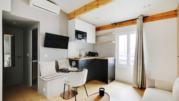 A modern kitchen with a microwave, stove, and sink. There is a dining area with a table and chairs. A TV is mounted on the wall. - Cosy Studio With AC -2p- Sacra-coeur Montmartre (Paris)