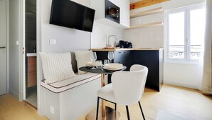 A compact living space with a kitchenette, a dining area with a table and chairs, and a TV mounted on the wall. - Cosy Studio With AC -2p- Sacra-coeur Montmartre (Paris)
