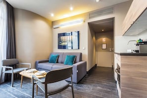 A modern living room with a sofa, chairs, a small table, and a kitchen area with a counter and sink.