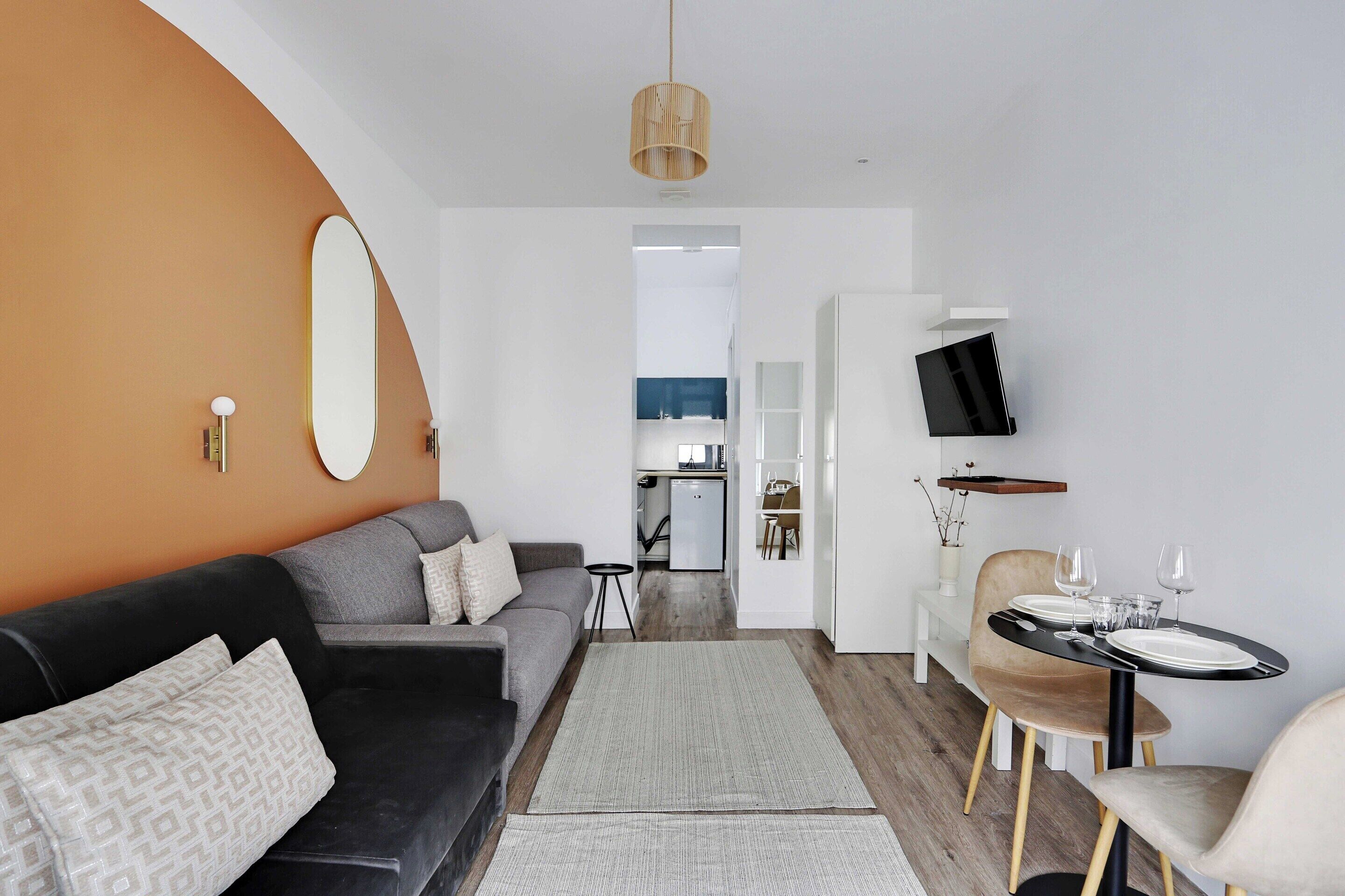A modern living room with a sofa, a dining table set for two, and a television mounted on the wall.