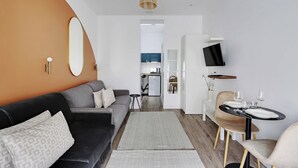 A modern living room with a sofa, a dining table set for two, and a television mounted on the wall. - Magnificent Studio - 2P - Near Bastille (Paris)