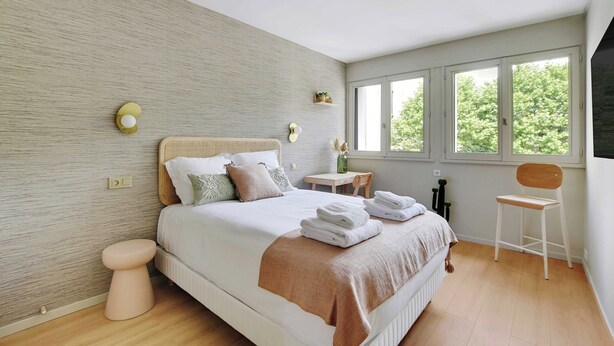 Una camera da letto con un letto, comodino, sedia e finestra vista alberi.
