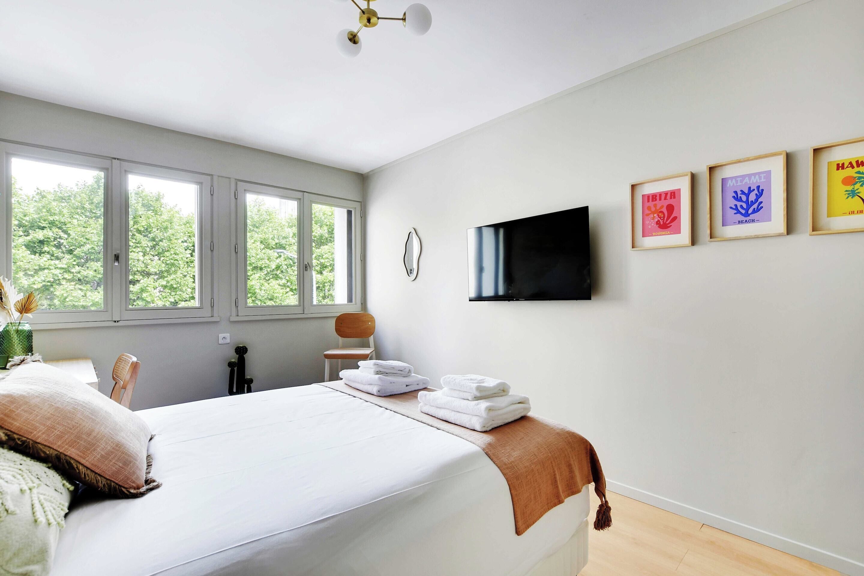 Ein Schlafzimmer mit einem großen Bett, einem flachbildfernseher an der Wand und drei gerahmten Bildern.