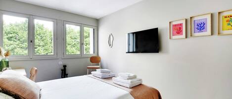 Ein Schlafzimmer mit einem großen Bett, einem flachbildfernseher an der Wand und drei gerahmten Bildern.