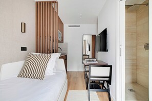 Et moderne hotelværelse med seng, skrivebord, stol, fjernsyn og brusebad.