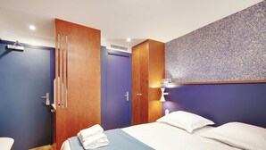 A hotel room with a bed, a wooden wardrobe, a blue door, and a wall-mounted light fixture. - Cosy Studio - 2P - Folie-mericourt (Paris)