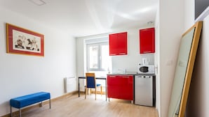 A compact kitchen with red cabinets, a microwave, and a sink. There is a blue bench and a chair in the room. - Magnificent Studio - 2P - Next to Paris (Malakoff)