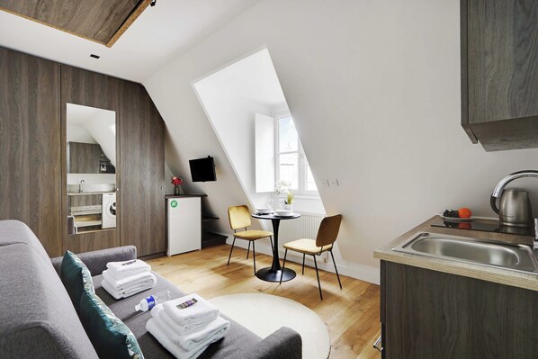 Un appartement moderne de style « loft », comprenant un coin repas, une kitchenette et une grande fenêtre laissant entrer la lumière naturelle.