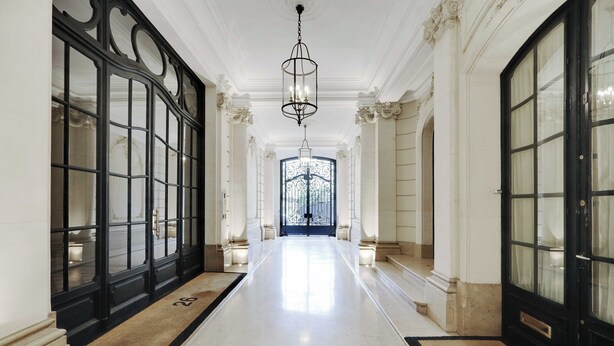 Un amplio pasillo con candelabro, ventanas grandes de marco negro y un felpudo con el número 26.