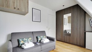 Una habitación moderna con un sofá gris, un armario de madera y una puerta blanca.