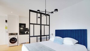 A modern bedroom with a large bed, a blue headboard, and a washing machine in the adjacent room. - Studio Sleek & Refined - Levallois-perret (Levallois-Perret)