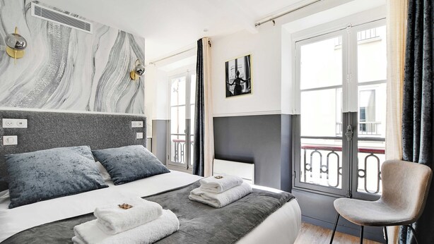 A modern hotel room with a large bed, a chair, a balcony, and a view of the city. - Cosy Studio for 2P With A/C - Near Montmartre (Paris)