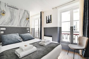 A modern hotel room with a large bed, a chair, a balcony, and a view of the city. - Cosy Studio for 2P With A/C - Near Montmartre (Paris)