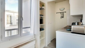 A compact kitchen with white cabinets, a countertop with a toaster, and a window with curtains. - Cosy Studio - 2P - Place de la Bastille (Paris)