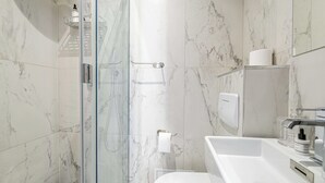 Ein modernes Badezimmer mit Duschkabine aus Glas, einem weißen Waschbecken und Wänden mit Marmorfliesen.