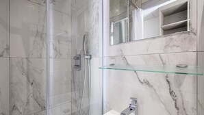 A bathroom with a glass shower enclosure, a white sink, and a marble-tiled wall. - Deluxe Bedroom With Balcony in Cannes Palais (Cannes)