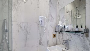 Un bagno moderno con cabina doccia in vetro, lavabo bianco e parete rivestita in marmo.