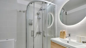 Ein modernes Badezimmer mit einer Duschkabine, einem weißen Waschbecken und einem Spiegel.