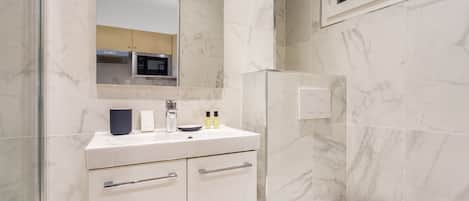 A bathroom with a white sink, mirror, and toilet. There is a glass shower enclosure and a window above the toilet.