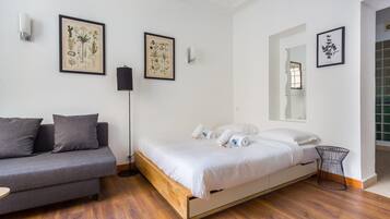 Un dormitorio con cama, sofá gris y una mesita. Las paredes están decoradas con láminas botánicas enmarcadas.