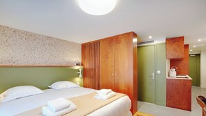 Ett hotellrum med en stor säng, en garderob i trä, ett litet pentry och en vägg som är accentfärgad i grönt.