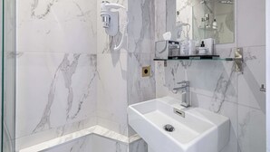A modern bathroom with a marble wall, a glass shower enclosure, a white sink, and a mounted hairdryer. - Hotel Avaton - Cosy Bedroom - Cannes Centre (Cannes)