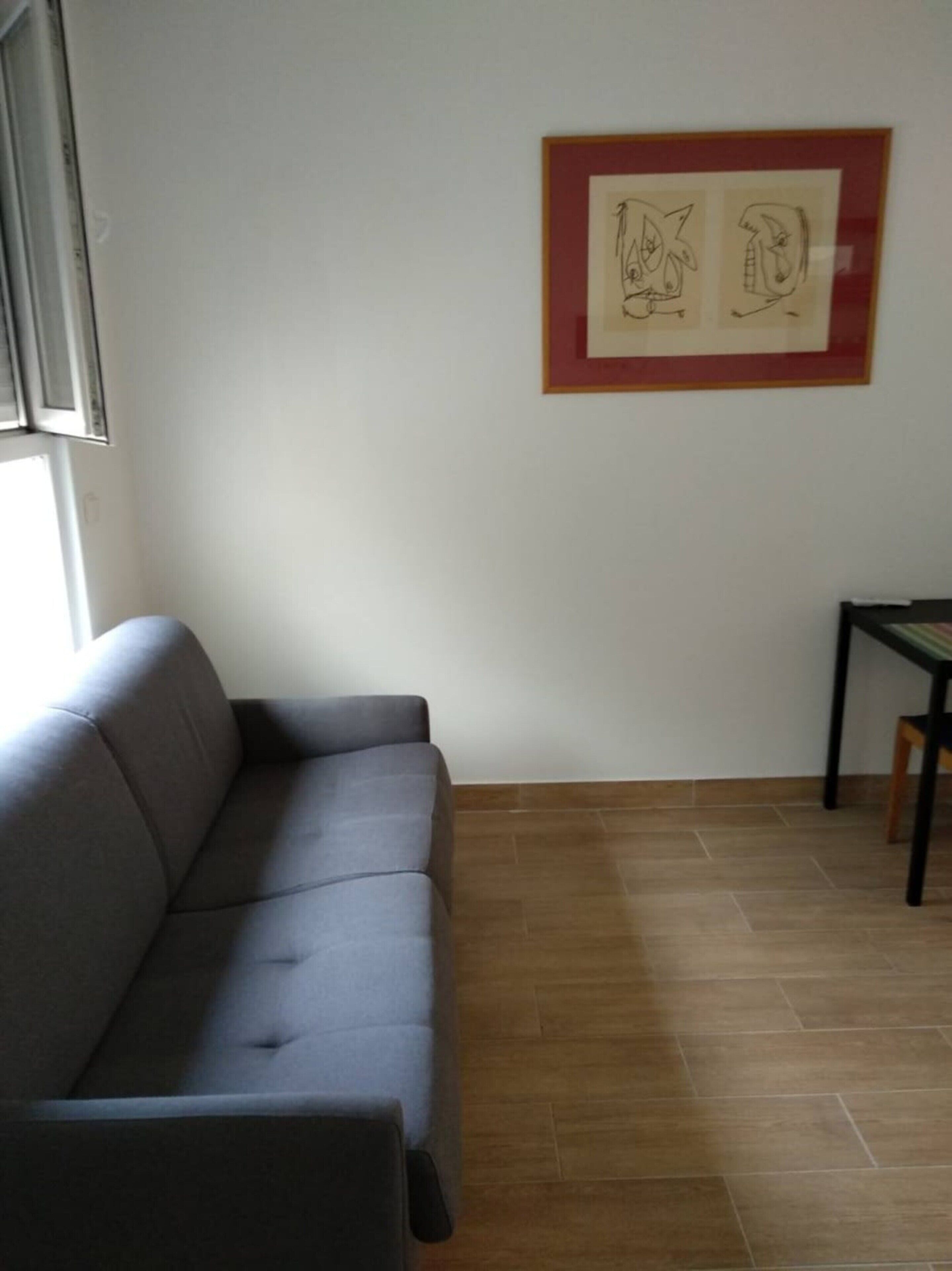 Una habitación con un sofá gris, una mesita y una obra de arte abstracto enmarcada en la pared.