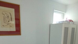 Uma pequena área de refeições com uma mesa, duas cadeiras, um armário branco e um quadro na parede.