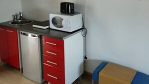 Cozinha compacta com armários vermelhos e brancos, micro-ondas, cafeteira e uma pia pequena.