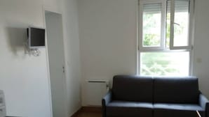 Um quarto com sofá cinza, armário de arquivo vermelho, televisão na parede e janela com persianas.