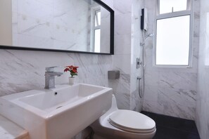 A bathroom with a white sink, a toilet, a shower, and a large mirror. - Cozy 1BR Suite at TriTower Steps to JB CIQ (Johor Bahru)