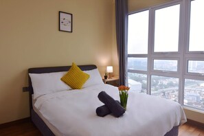 Een netjes opgemaakt bed met een witte deken, een opgerolde handdoek en een vaas met bloemen.