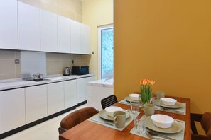 A modern kitchen with white cabinets, a dining table set with plates, bowls, and glasses, and a window with a view. - Cozy 1BR Suite at TriTower Steps to JB CIQ (Johor Bahru)