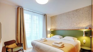 A hotel room with a large bed, a chair, a small table, and a wall clock. - Elegant Studio - 2P - Republique (Paris)