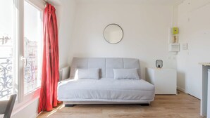 Une chambre à coucher avec un lit, une fenêtre ornée de rideaux rouges, un miroir rond accroché au mur et une table de chevet avec une lampe.