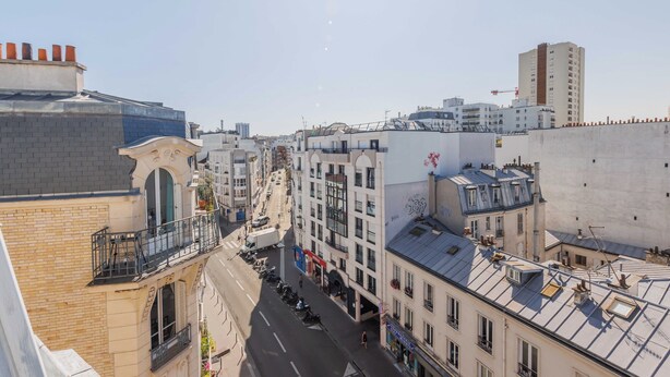Un paysage urbain où se côtoient une architecture moderne et traditionnelle, avec notamment un immeuble doté d’un balcon imposant et un autre avec une grande fenêtre.