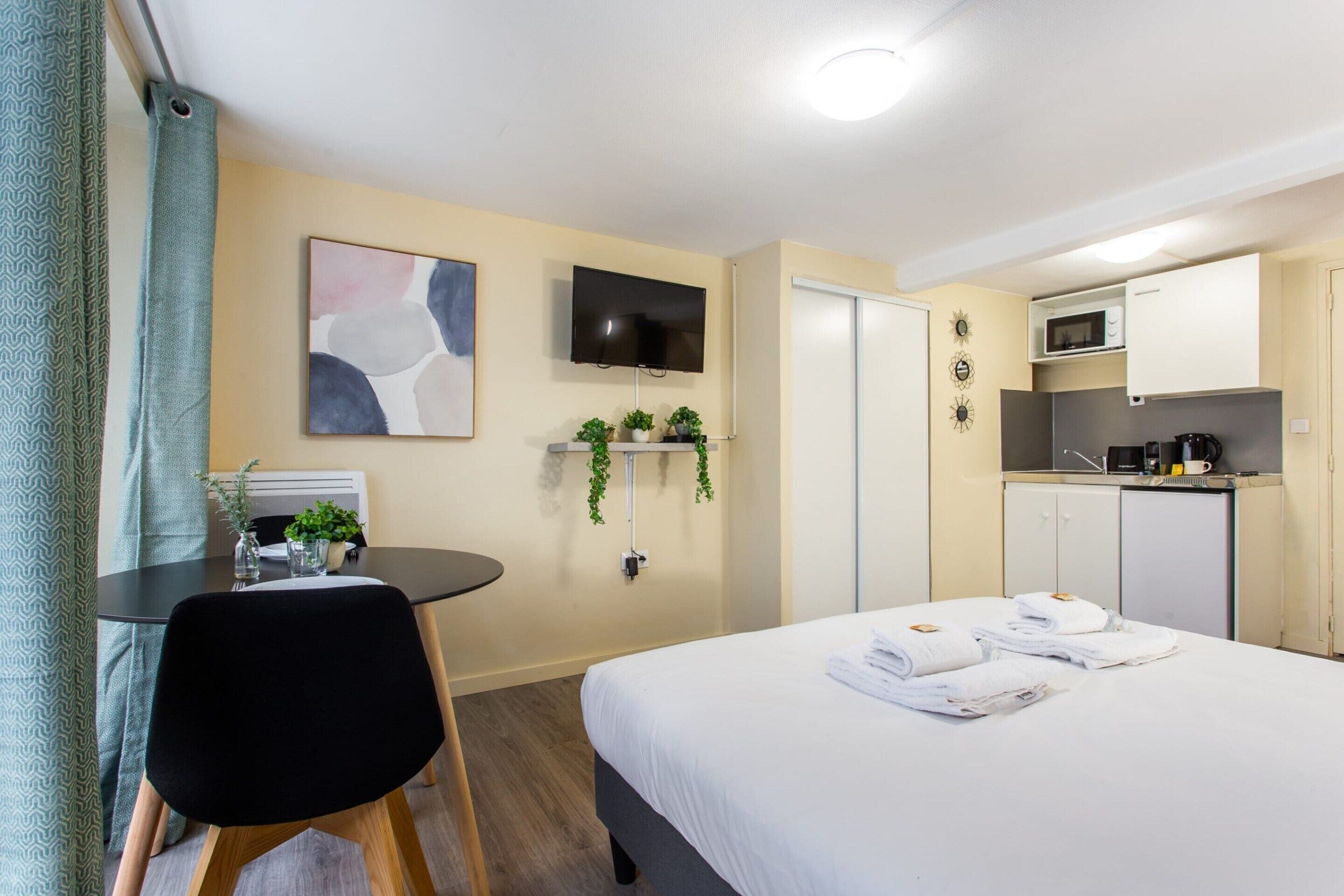A hotel room with a bed, a desk, a chair, a TV, a microwave, and a small kitchen area.