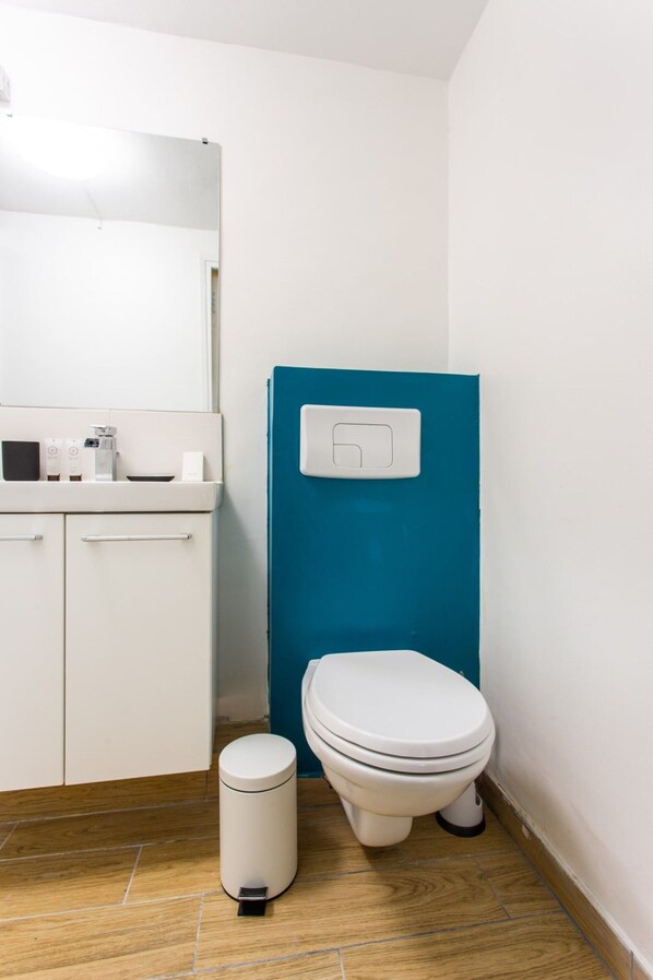 A small bathroom with a white toilet, a blue wall, a white sink, and a trash bin.