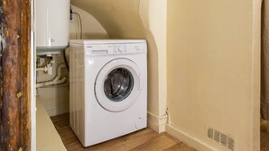 Uma lavanderia compacta com máquina de lavar frontal, aquecedor de água e piso de madeira.