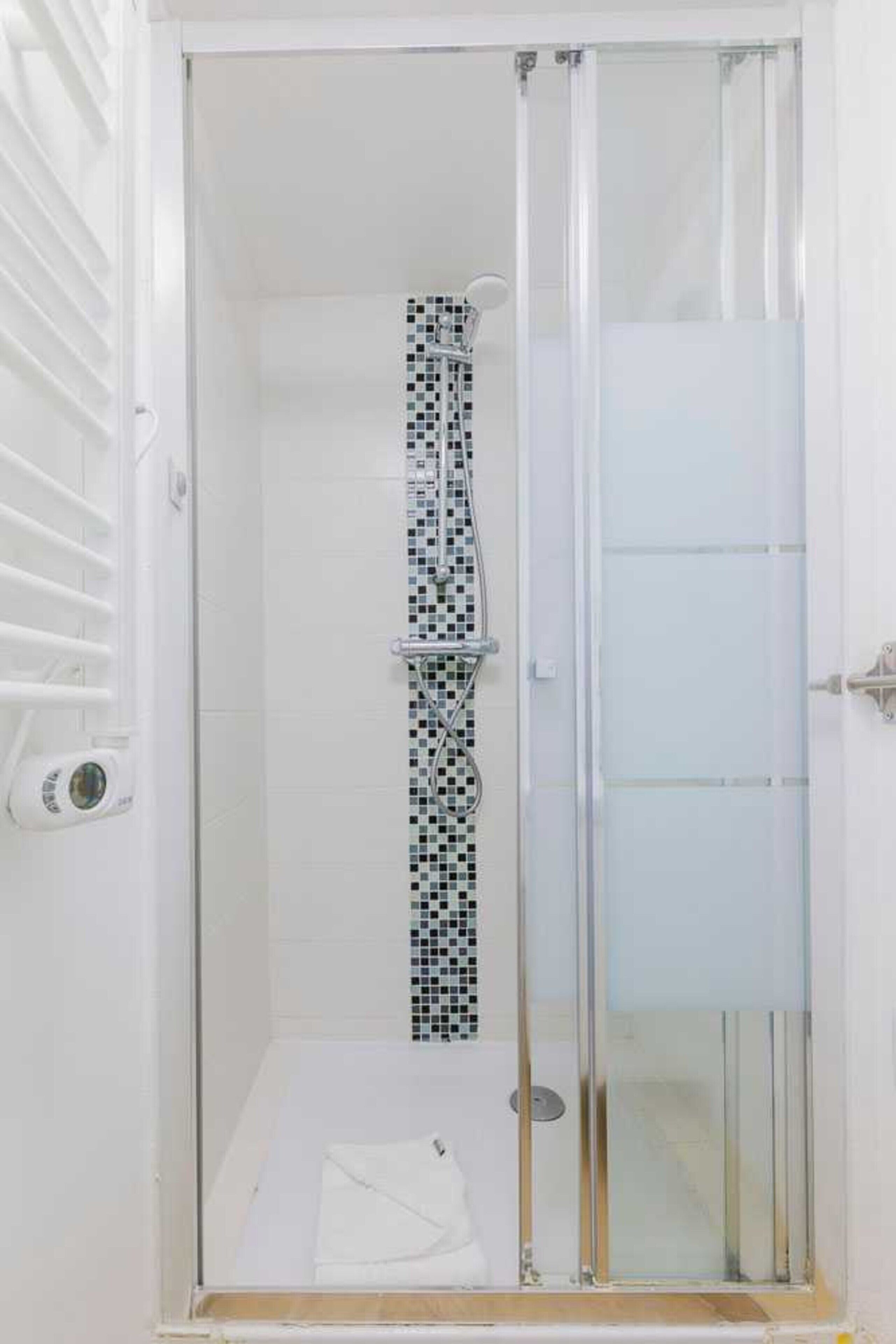 A glass-enclosed shower with a tiled wall and a white door.