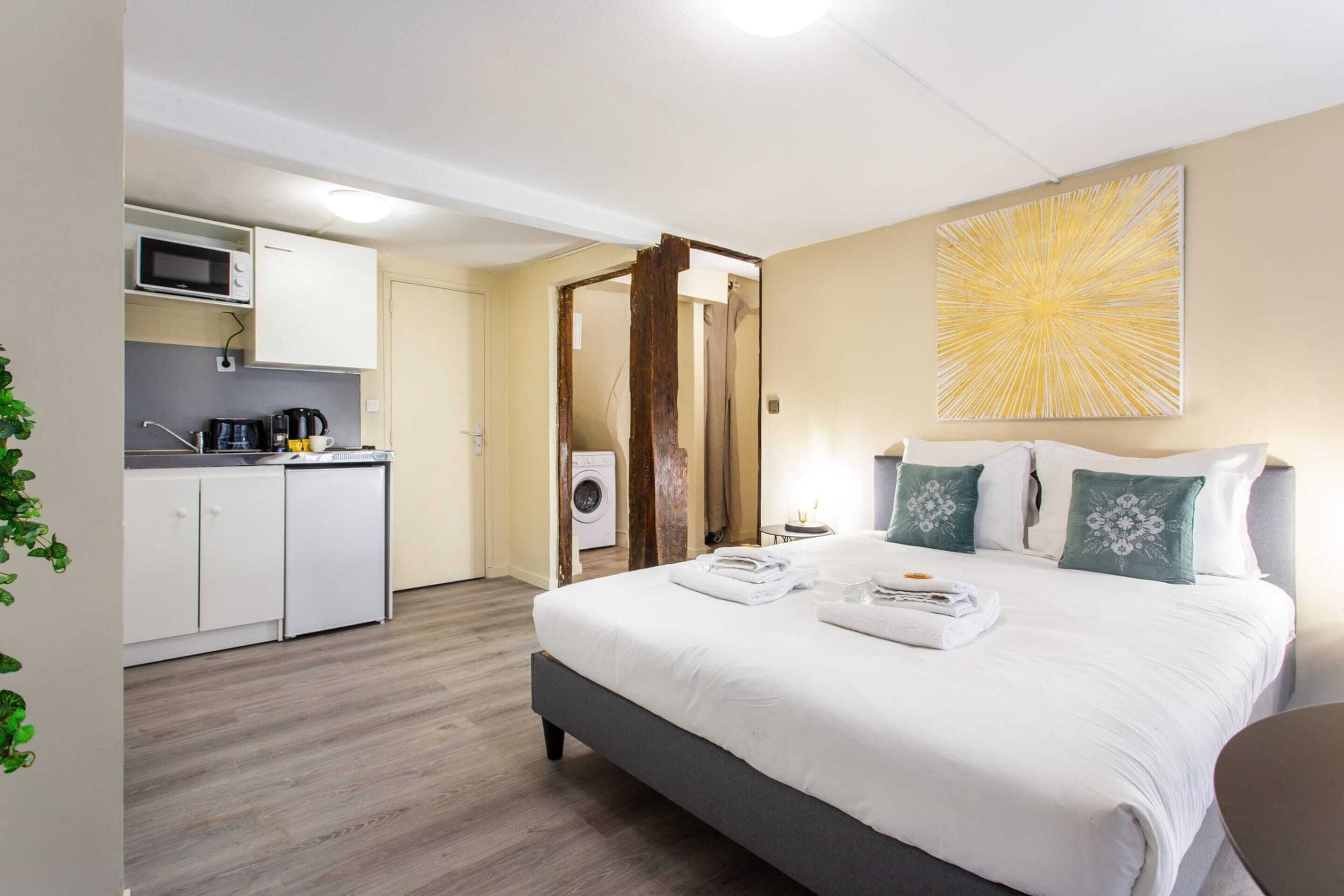 A hotel room with a bed, a desk, a microwave, a coffee maker, and a washing machine.