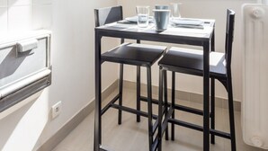 A dining area with a table and chairs, a window with a view, and a kitchen area with a stove. - Superbe Studio - 4P - Trocadero (Paris)