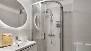 Un baño moderno con ducha de vidrio, lavamanos con espejo y un inodoro.